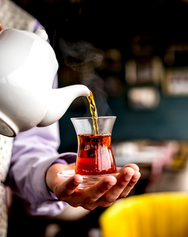 side-view-person-pouring-black-tea-from-white-ceramic-teapot-into-armudu-glass side-view-person-pouring-black-tea-from-white-ceramic-teapot-into-armudu-glass
